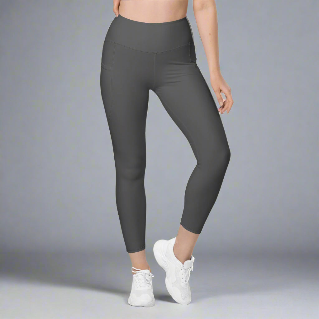 Person wearing dark gray leggings and white sneakers on a gray background